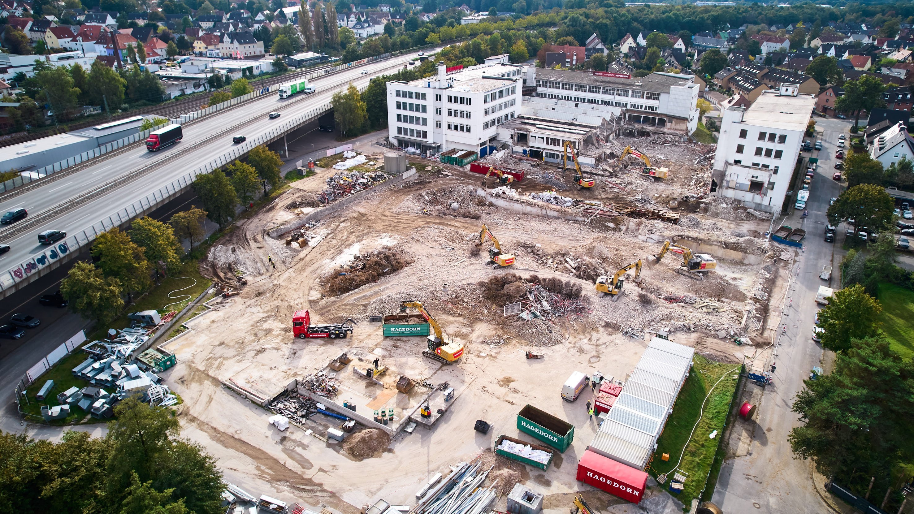 Luftbild von Abrissarbeiten auf einem großen Gelände neben einer Stadtstraße und Wohngebieten.