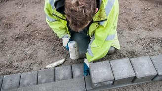 Arbeiter in Warnkleidung verlegt Pflastersteine auf einer Baustelle.