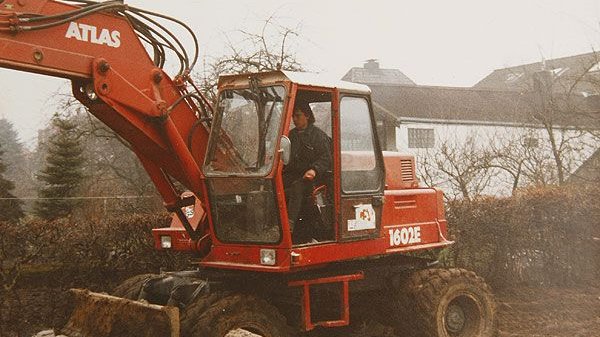 Arbeiter bedient roten Bagger auf Baustelle.