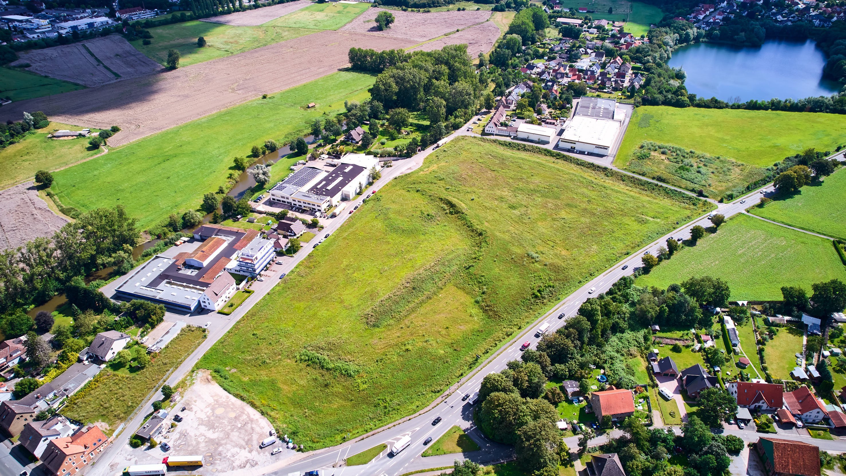 Luftbild von einer grünen, unbebauten Fläche umgeben von Straßen und Gebäuden in einer ländlichen Gegend.