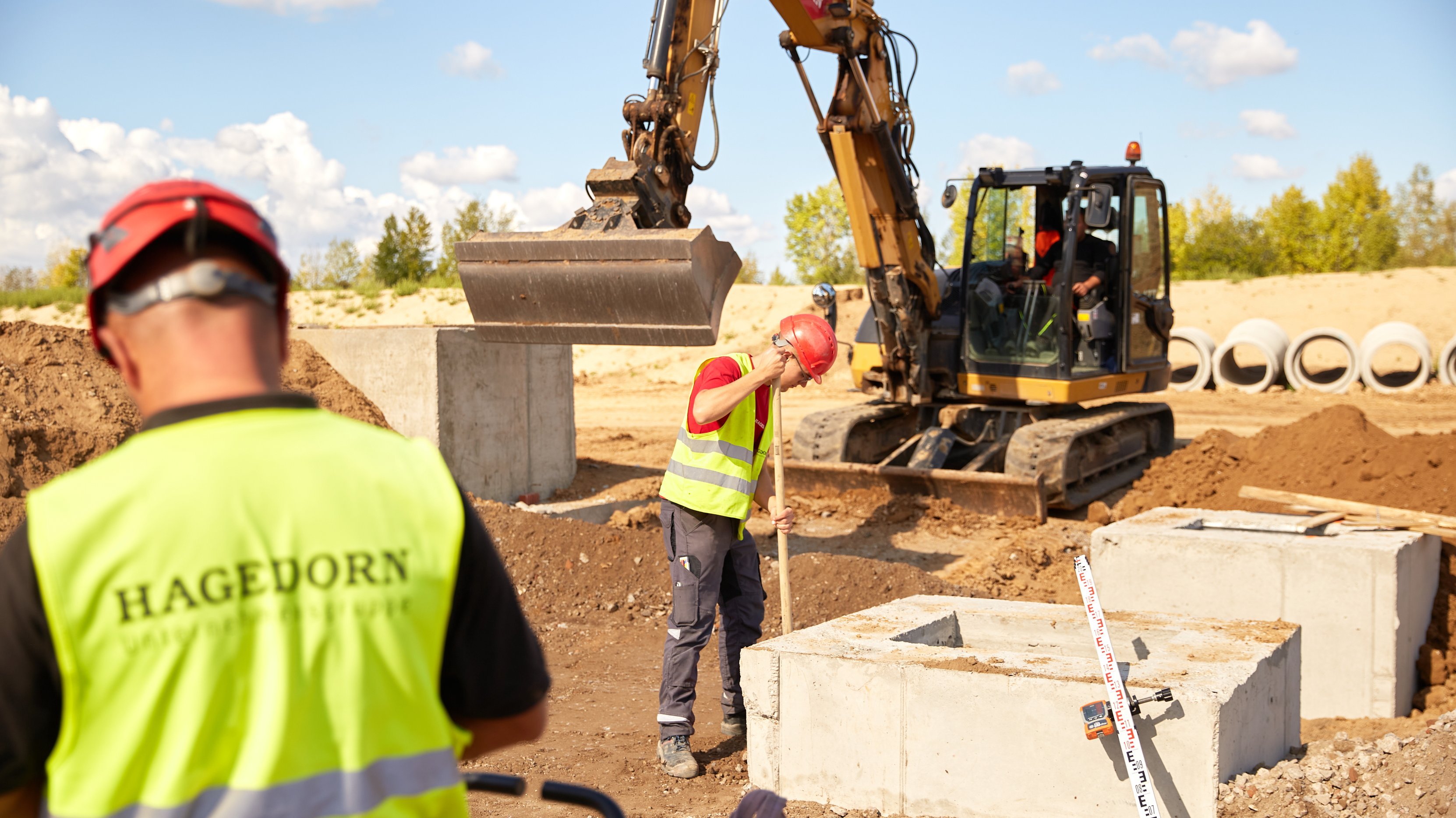 Arbeiter und Bagger koordinieren Arbeit bei Fundamentlegung.