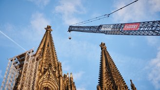 Kran mit Hagedorn-Banner über historischer Kirchenbaustelle.