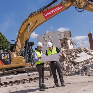 Planung und Überwachung des Abrisses durch Fachpersonal mit Bauplänen vor einem Bagger.