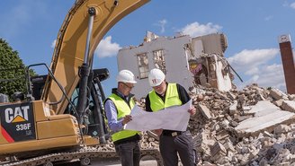 Experten analysieren Statik auf Baustelle mit Bagger und Ruinen.