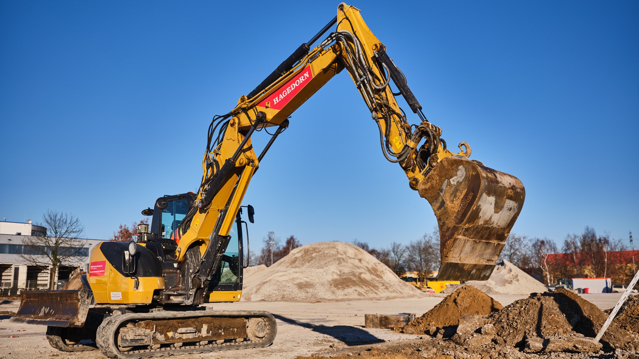 Bagger lädt Schutt in sonniger Baustellen-Umgebung.
