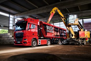 Entsorgungsprozess mit Bagger und Kipplaster in einer Recyclinganlage.