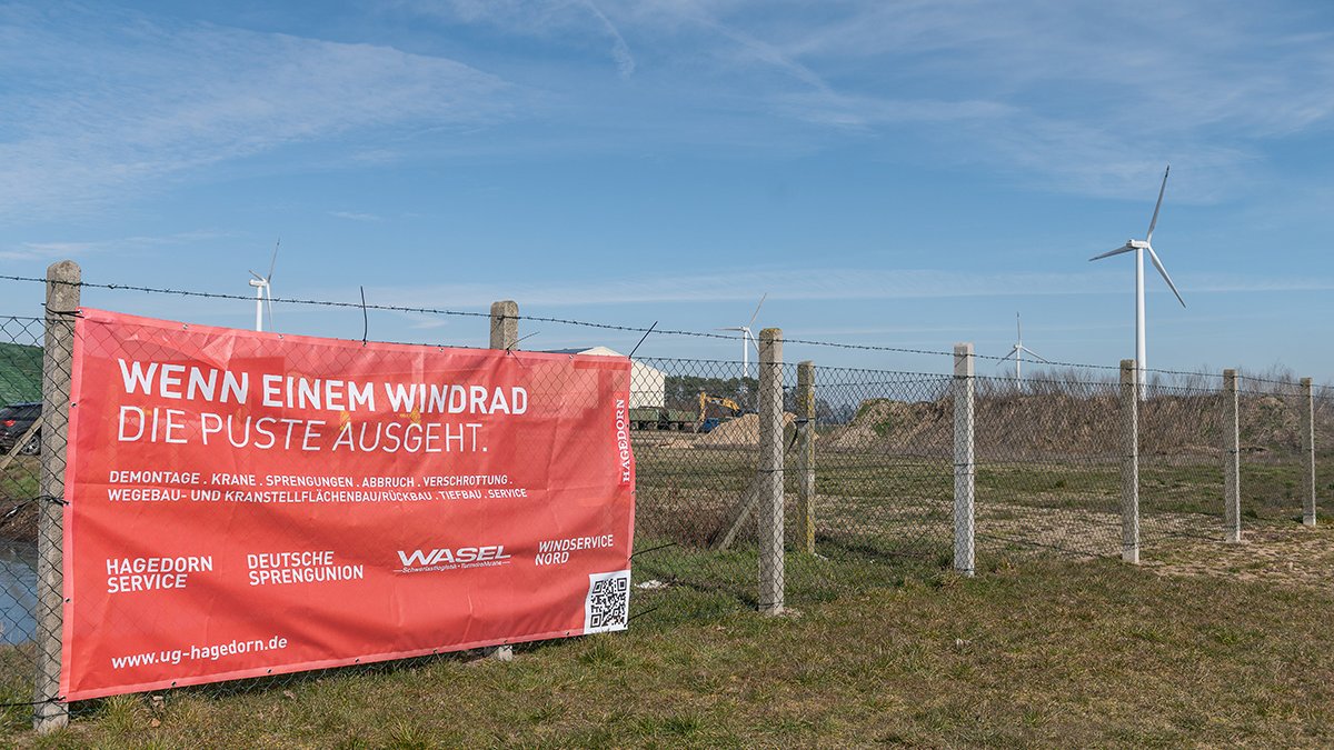 Informationsbanner an einem Zaun vor Windkraftanlagen