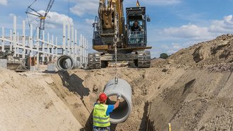 Bauarbeiter und Maschinen bei der Installation von Kanalrohren.