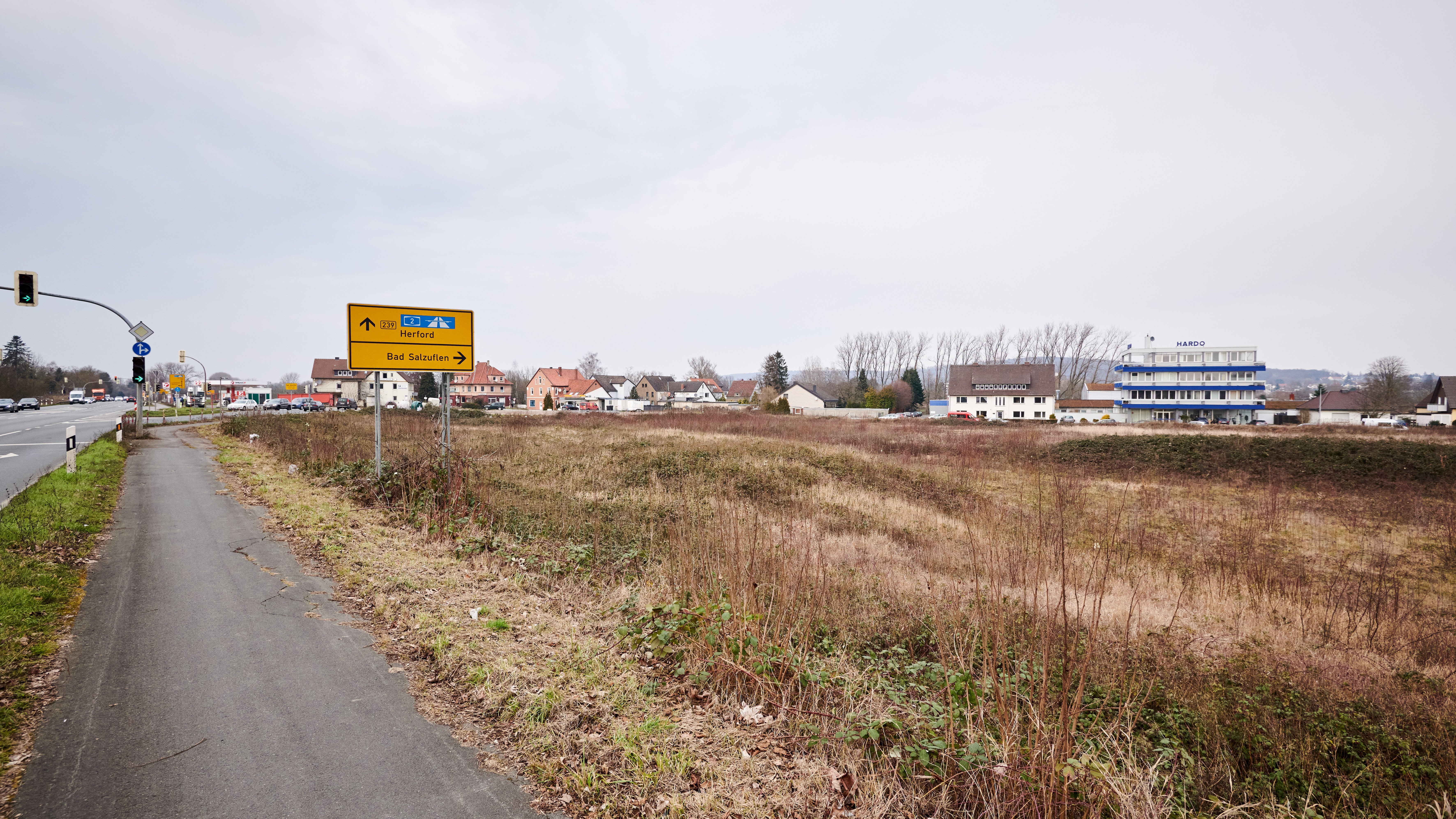 Leeres Grundstück neben einer Hauptstraße, umgeben von städtischen und gewerblichen Gebäuden.