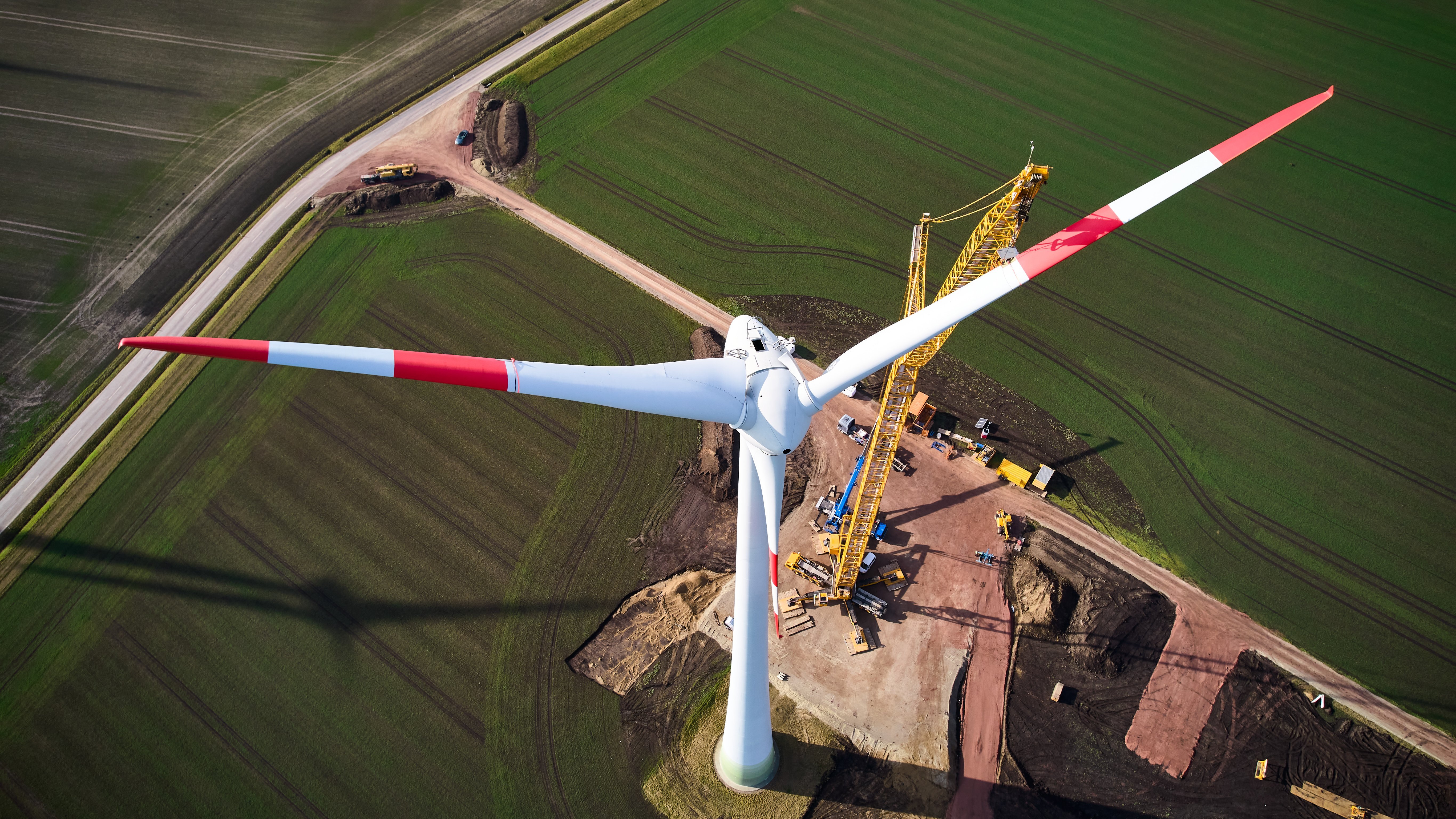 Arbeiter demontieren Windradflügel mit Kran auf ländlichem Grundstück.