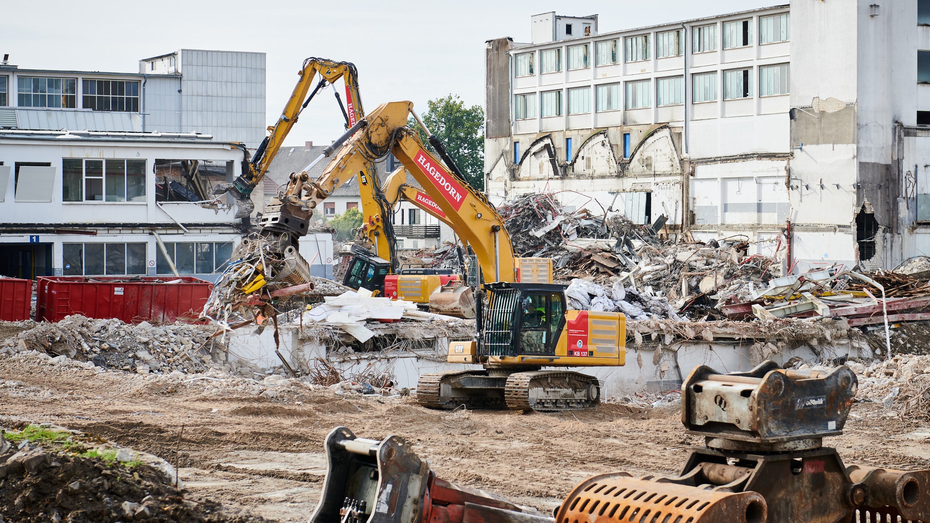 Zwei gelbe Bagger beim systematischen Abbruch eines mehrstöckigen Industriegebäudes in der Stadt.